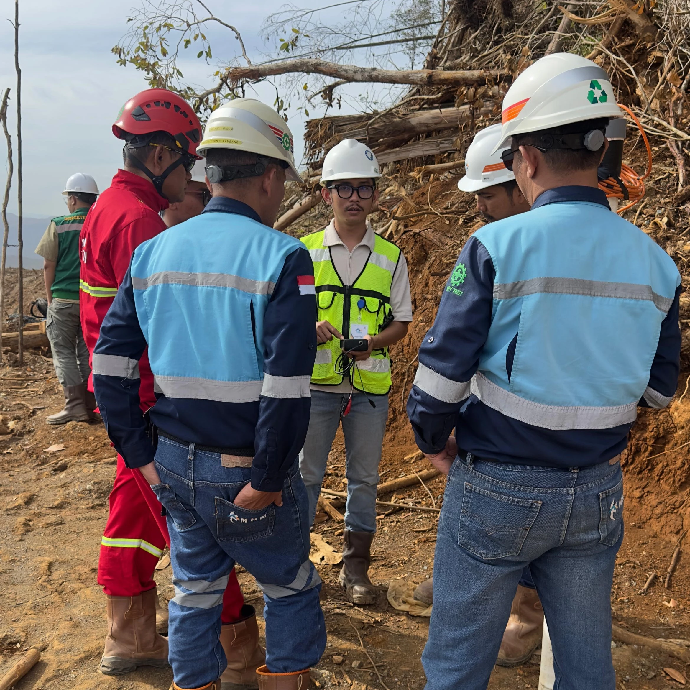 Tim instalasi dan klien berdiskusi teknis di dekat piezometer di lokasi tambang Kalimantan, meninjau data pada pembaca genggam di tengah lapangan terbuka.