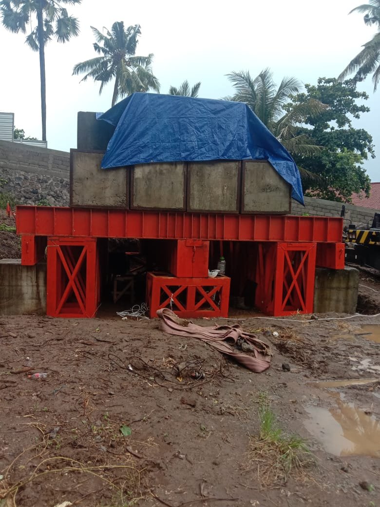 Pemandangan sisi depan bagian bawah platform baja oranye penyangga beban uji Kentledge di area berlumpur.