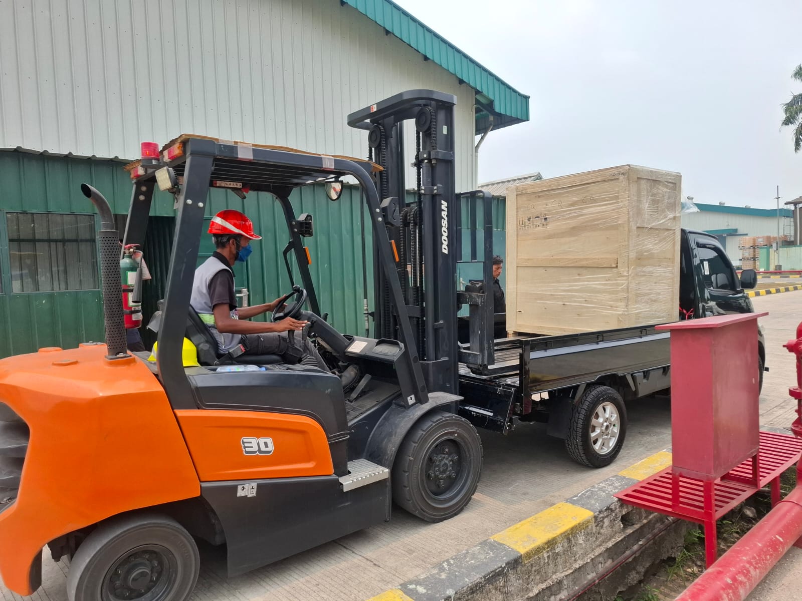 Forklift dan operator berada di samping pikap dengan peti kayu besar di baknya